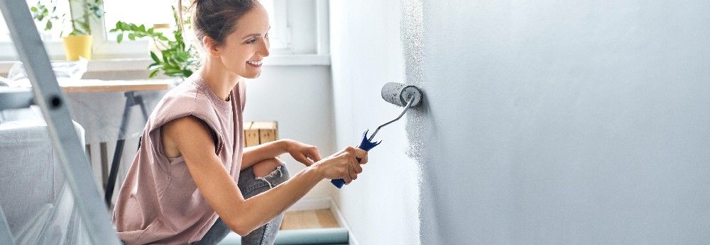 Eine Frau streicht eine Zimmerwand mit grauer Strukturfarbe.